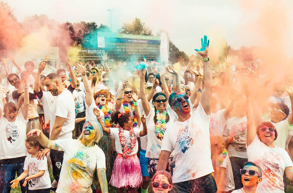 colour run photo with thousands of runners throwing colour powder in the air at the warm up area of a colour run charity event.