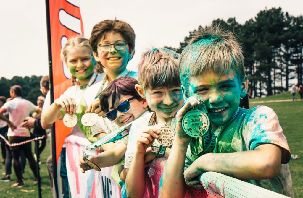 children holding wooden medals for a colour run. Colour powder all over the childrens t-shirts and faces as they proudly show off the eco-friendly wooden medals from a colour run in the UK.